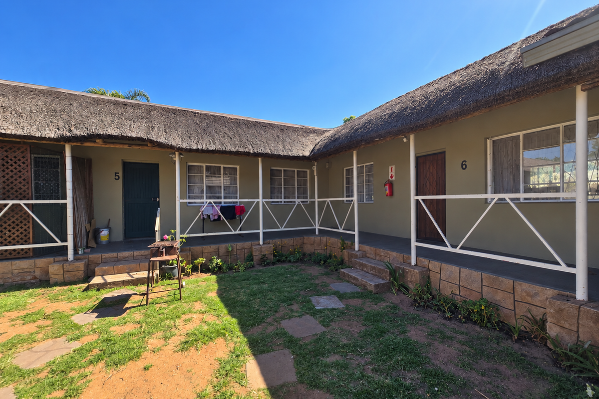 Exterior view of retirement village units featuring thatch roofing, stone-clad foundations, and a shared walkway overlooking a garden area.