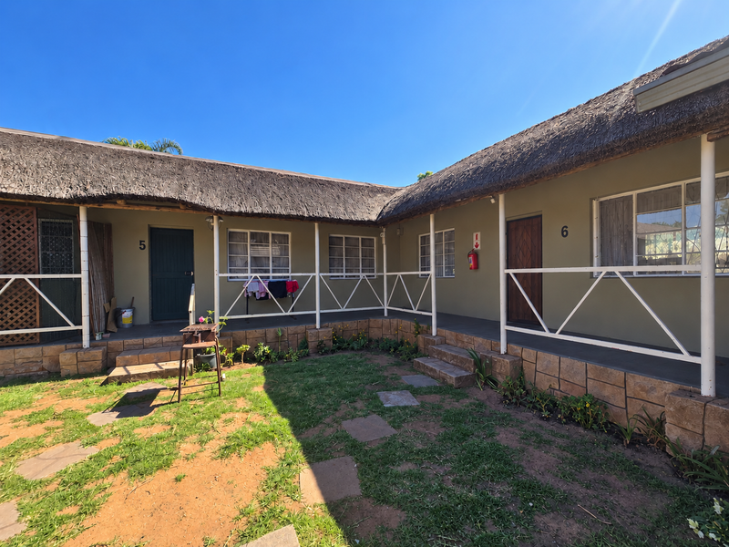 Exterior view of retirement village units featuring thatch roofing, stone-clad foundations, and a shared walkway overlooking a garden area.