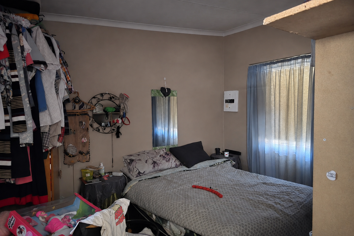 A bedroom featuring a window with curtains and a wall-mounted electrical distribution board.