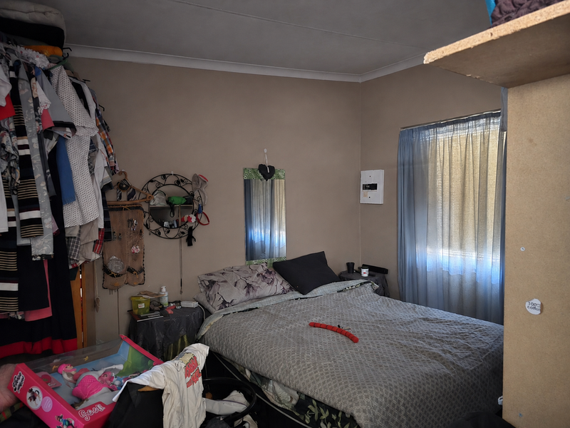 A bedroom featuring a window with curtains and a wall-mounted electrical distribution board.