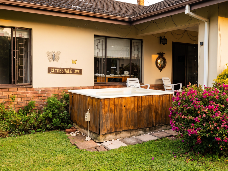 Rear exterior view featuring a covered patio area, established garden, and a built-in jacuzzi set against the house facade.
