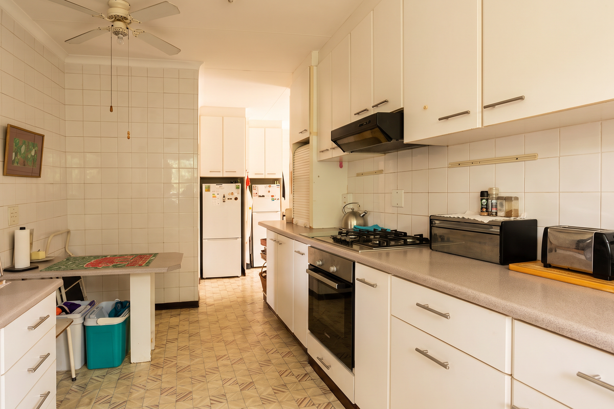 A functional kitchen featuring white cabinetry, a gas hob, built-in oven, extractor fan, and tiled splashbacks with a classic layout.