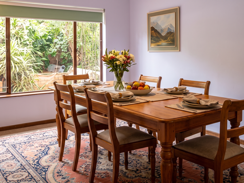 A dining room featuring a large window with security bars and a roller blind, providing natural light and a view of the garden.