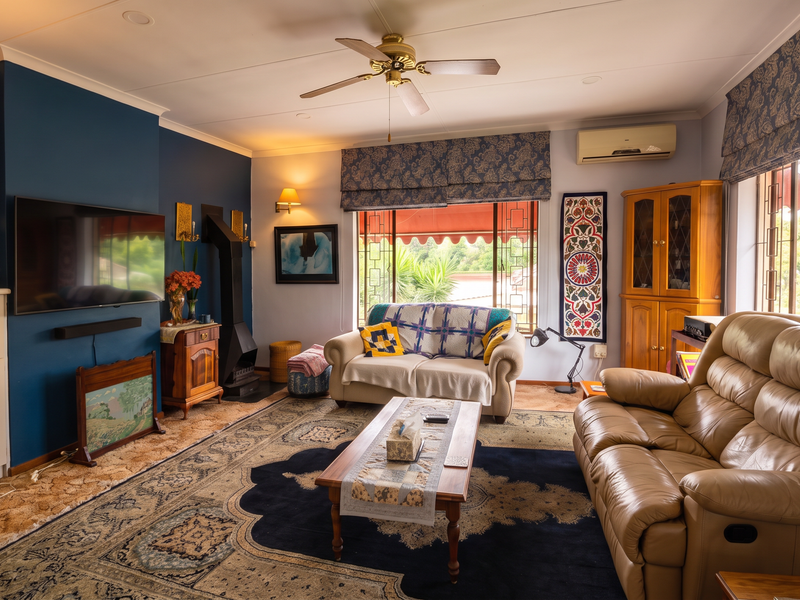 A comfortable living room featuring a built-in fireplace, ceiling fan, and wall-mounted air conditioning unit, offering a cozy and functional space.
