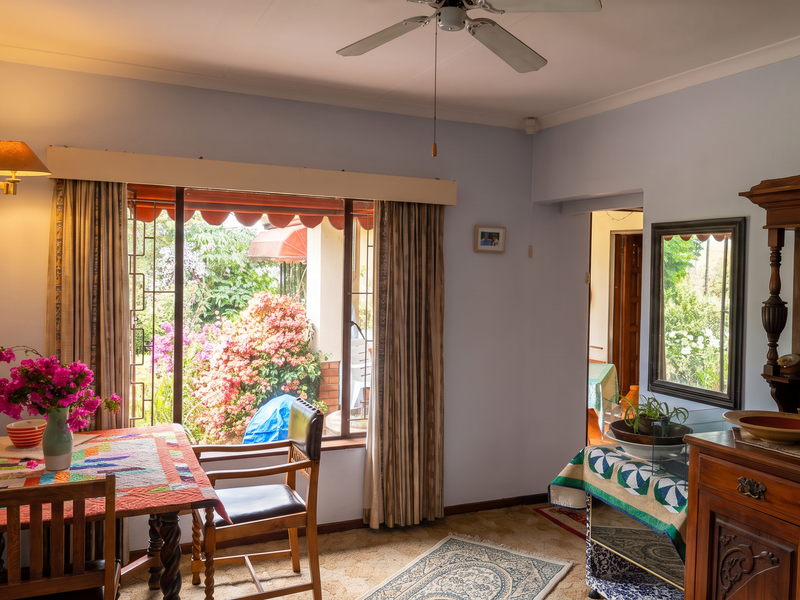 A cozy living area featuring a ceiling fan, carpeted flooring, and a large window providing natural light and views of the garden.