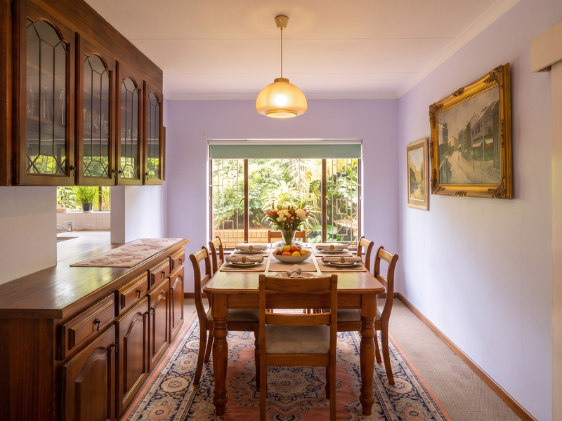 A dining room featuring built-in wooden cabinetry, a pendant light, and a large window overlooking the garden, providing a functional and traditional space.