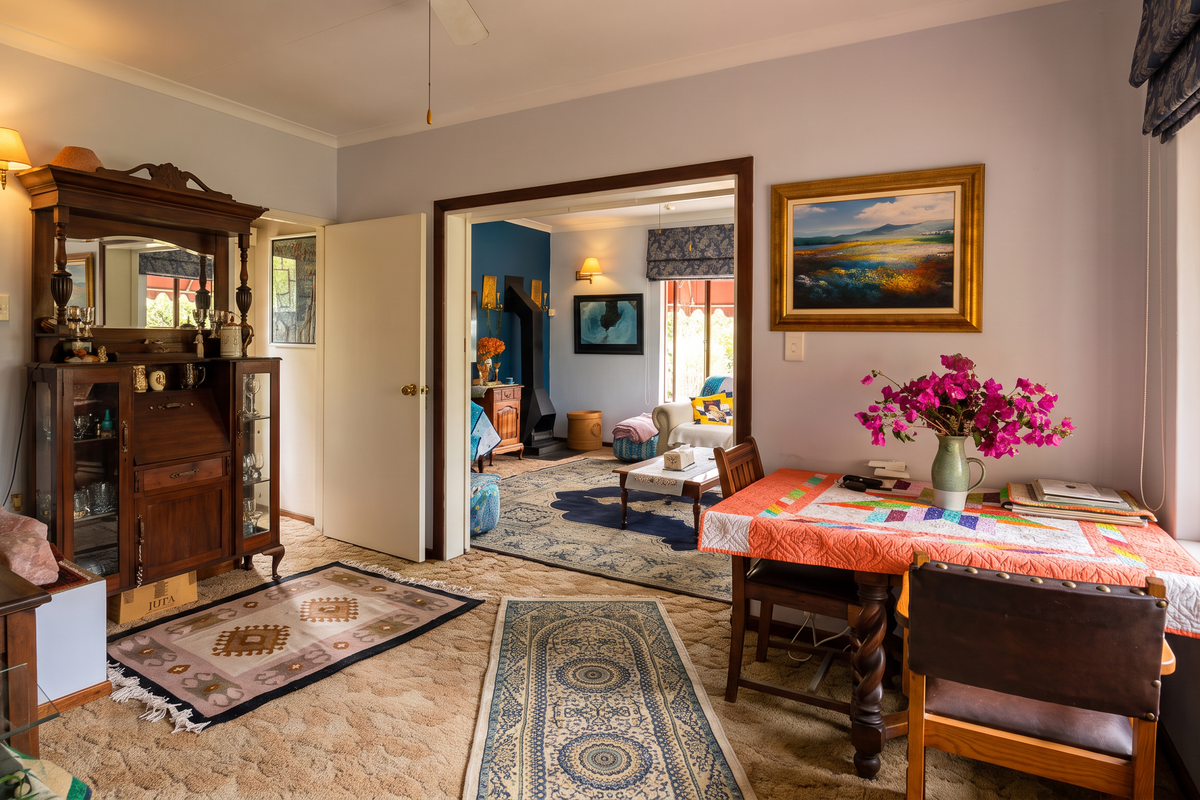 A cozy living area featuring carpeted flooring, timber window frames, and an open-plan flow into an adjacent room with a fireplace.