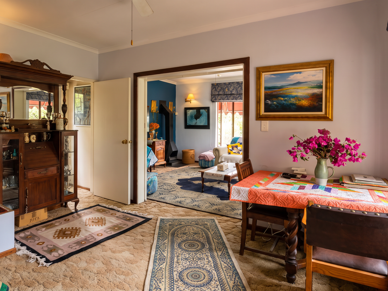 A cozy living area featuring carpeted flooring, timber window frames, and an open-plan flow into an adjacent room with a fireplace.