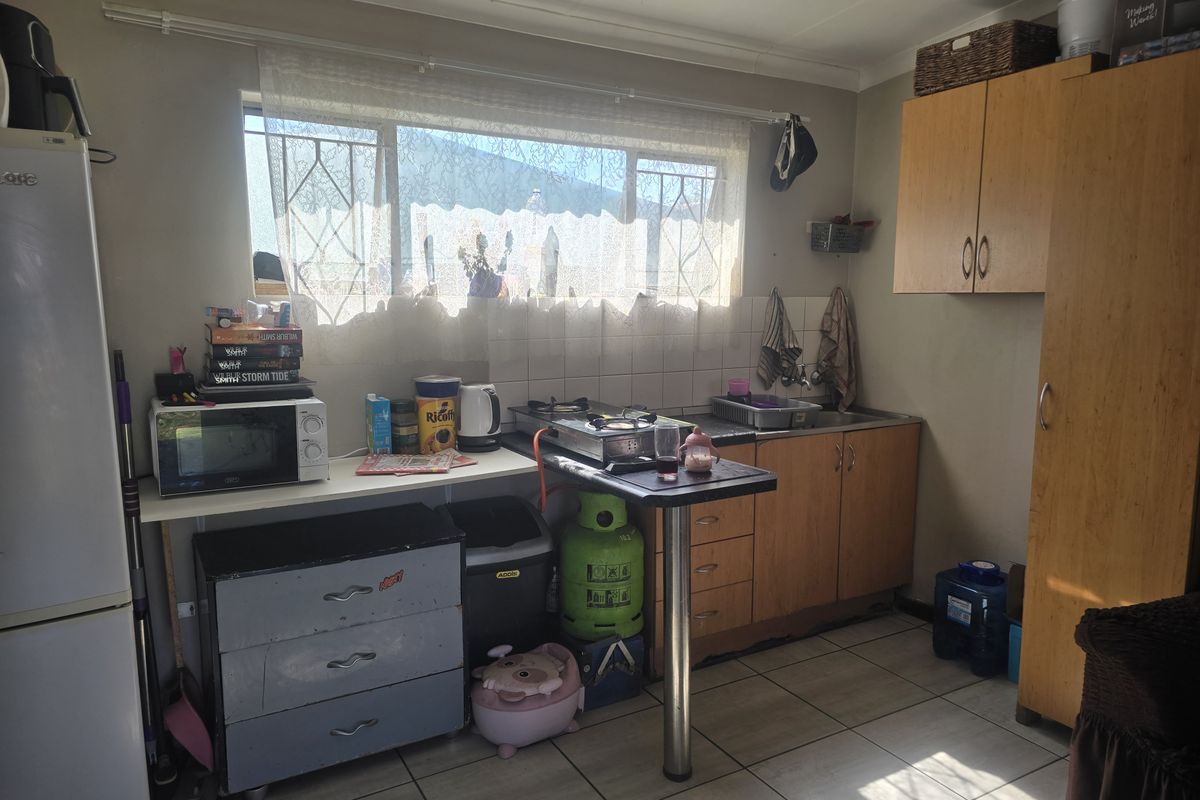 A compact kitchen featuring built-in wooden cabinetry, tiled flooring, and a stainless steel sink, offering a functional space in need of cosmetic updates.