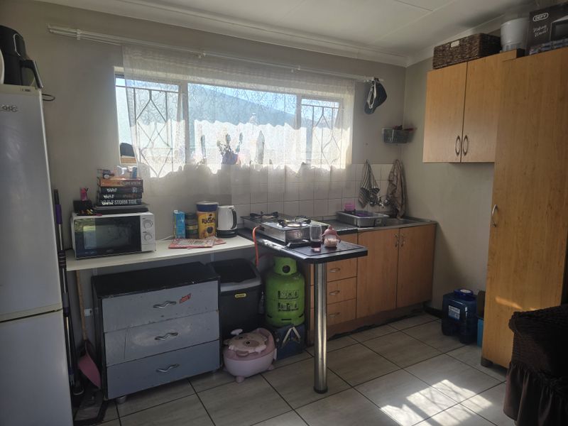 A compact kitchen featuring built-in wooden cabinetry, tiled flooring, and a stainless steel sink, offering a functional space in need of cosmetic updates.