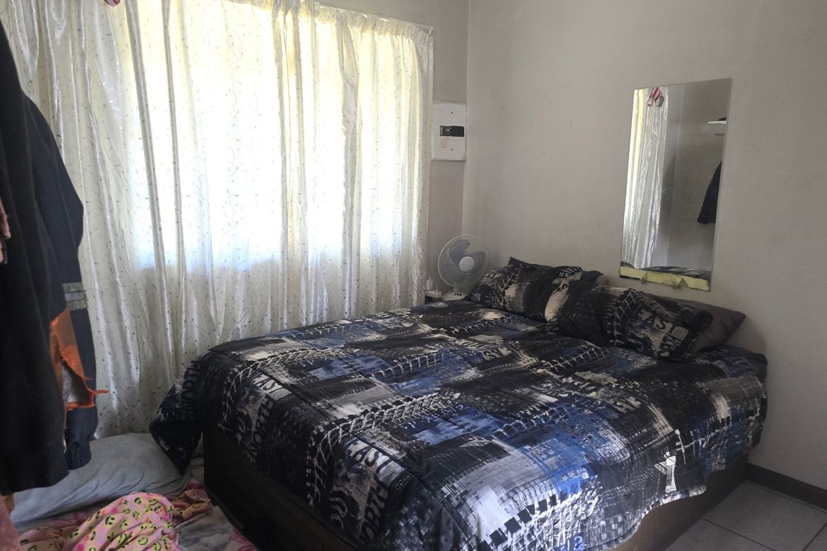 A functional bedroom featuring tiled flooring and a wall-mounted electrical distribution board, providing a basic and practical living space.