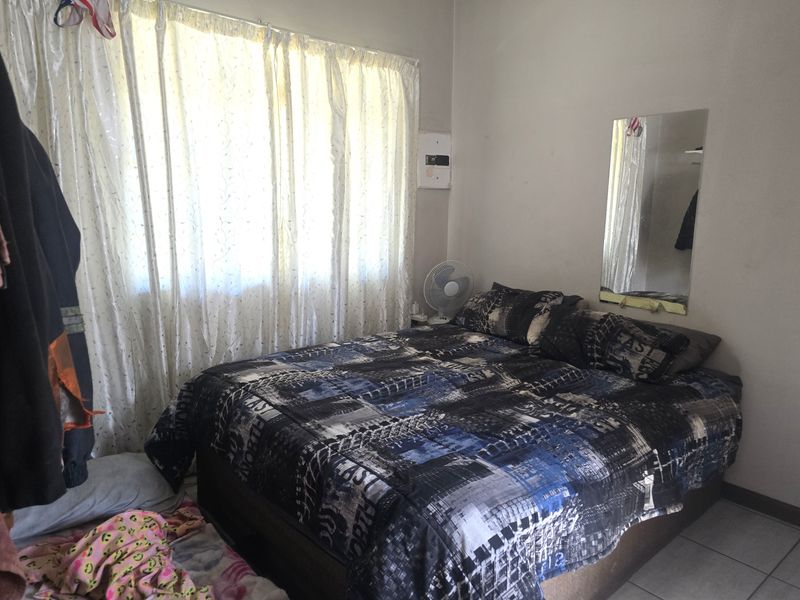 A functional bedroom featuring tiled flooring and a wall-mounted electrical distribution board, providing a basic and practical living space.
