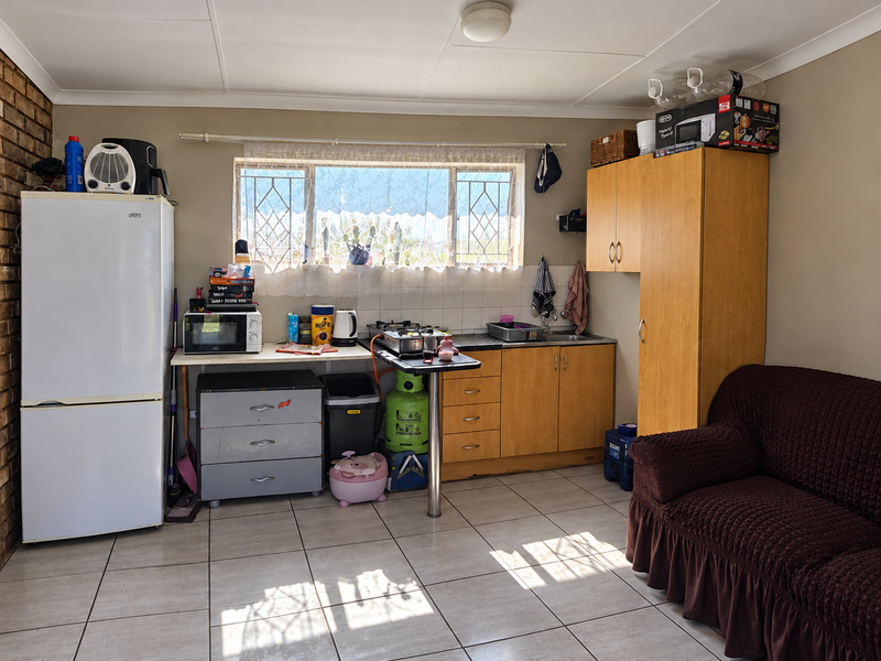 Open plan kitchen area featuring tiled floors, built-in wooden cabinetry, a brick feature wall, and security-fitted windows, offering a functional layout for retirement living.