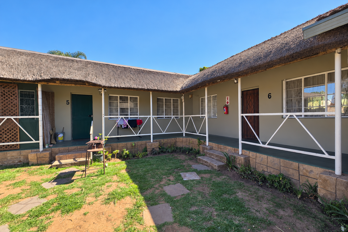 Exterior view of retirement village units featuring a shared covered veranda, thatched roofing, and stone-clad base with direct garden access.