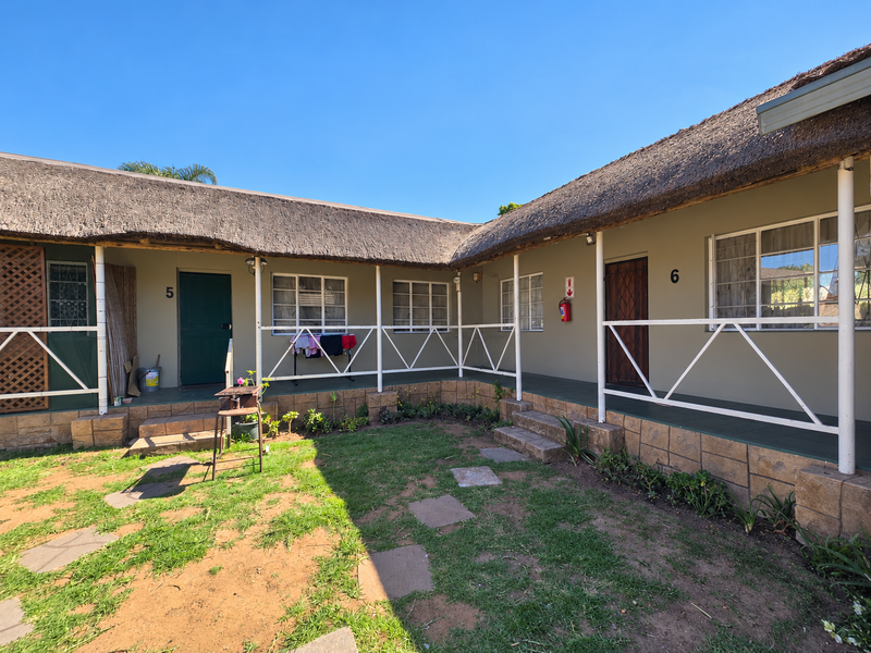 Exterior view of retirement village units featuring a shared covered veranda, thatched roofing, and stone-clad base with direct garden access.