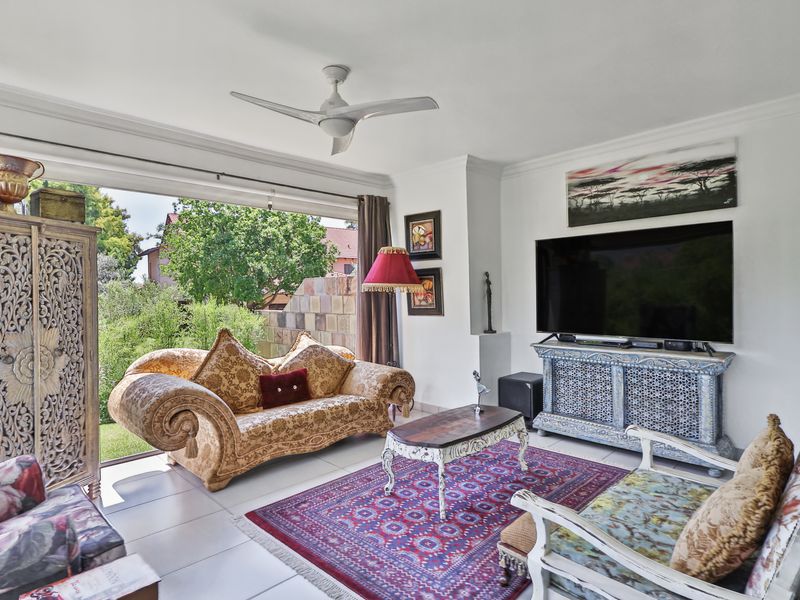 A bright living room featuring tiled flooring, a ceiling fan, and a large sliding glass door that opens to a garden view.
