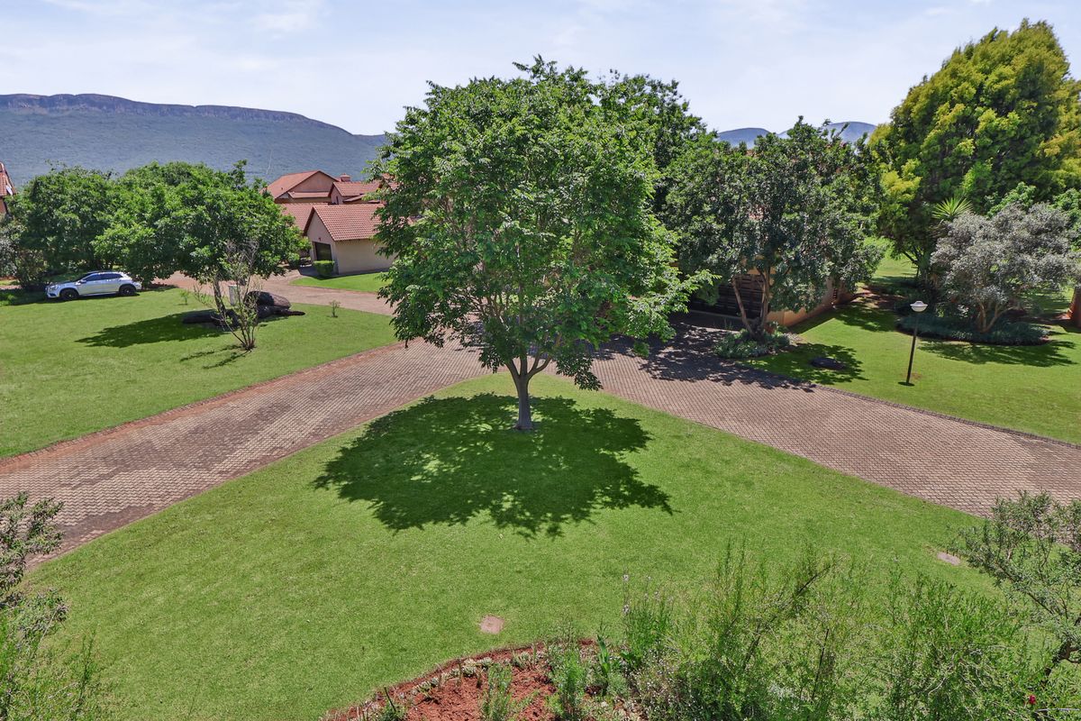 An aerial view of the property grounds featuring a well-maintained lawn, mature trees, and a paved driveway leading towards the townhouse complex.