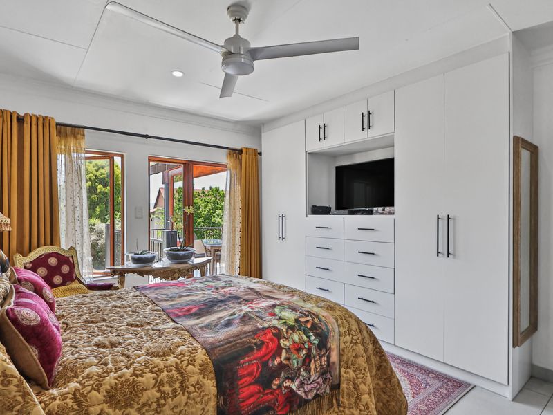 Spacious bedroom featuring extensive built-in cabinetry with integrated storage and drawers, a ceiling fan, and direct access to an outdoor balcony through sliding doors.