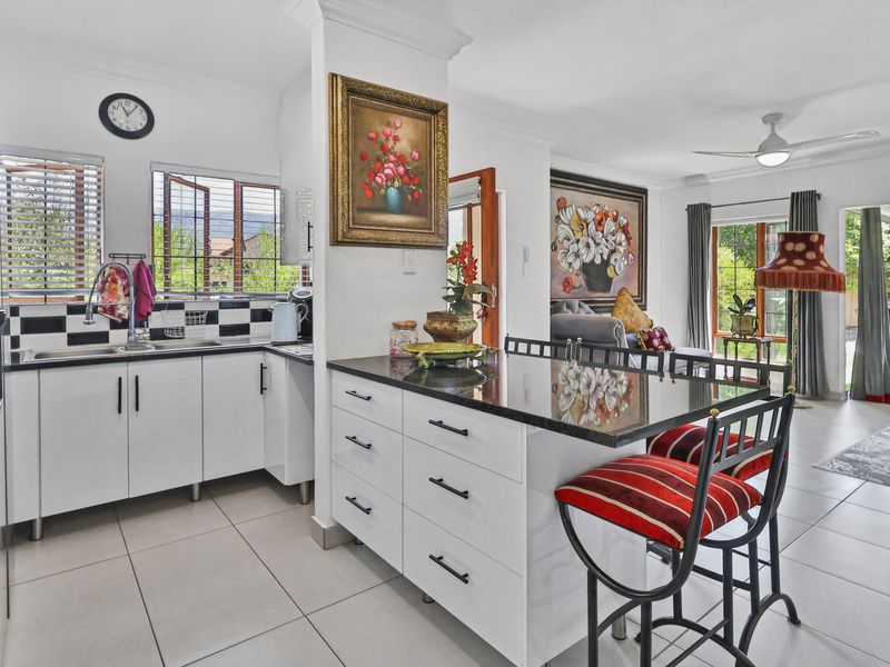 Open-plan kitchen and living area featuring a central island with granite countertops, white cabinetry, and tiled flooring, flowing into a bright lounge space.