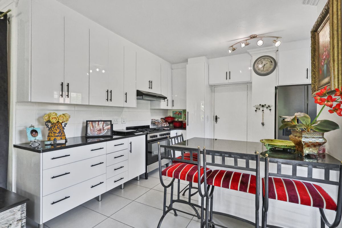 Modern kitchen featuring white gloss cabinetry, black stone countertops, gas stove, extractor fan, and a convenient breakfast bar with tiled flooring.