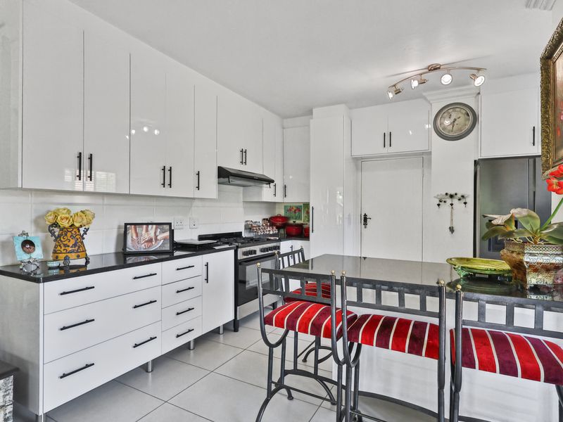 Modern kitchen featuring white gloss cabinetry, black stone countertops, gas stove, extractor fan, and a convenient breakfast bar with tiled flooring.