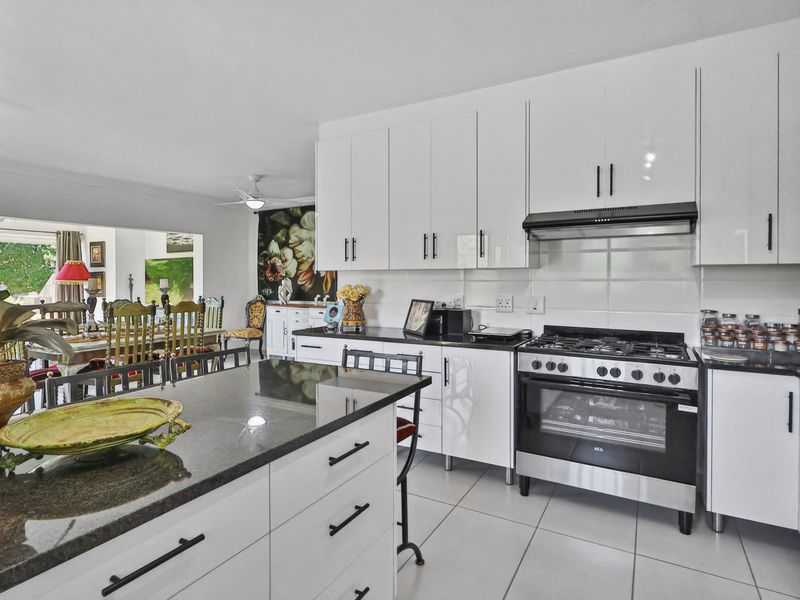 Modern open-plan kitchen featuring white gloss cabinetry, granite countertops, and a gas stove, seamlessly flowing into the adjacent dining area.