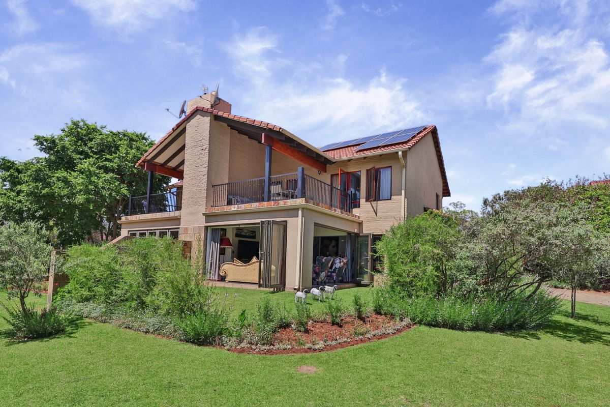 Rear view of a two-story townhouse featuring a balcony, bi-fold doors opening to the garden, and roof-mounted solar panels.