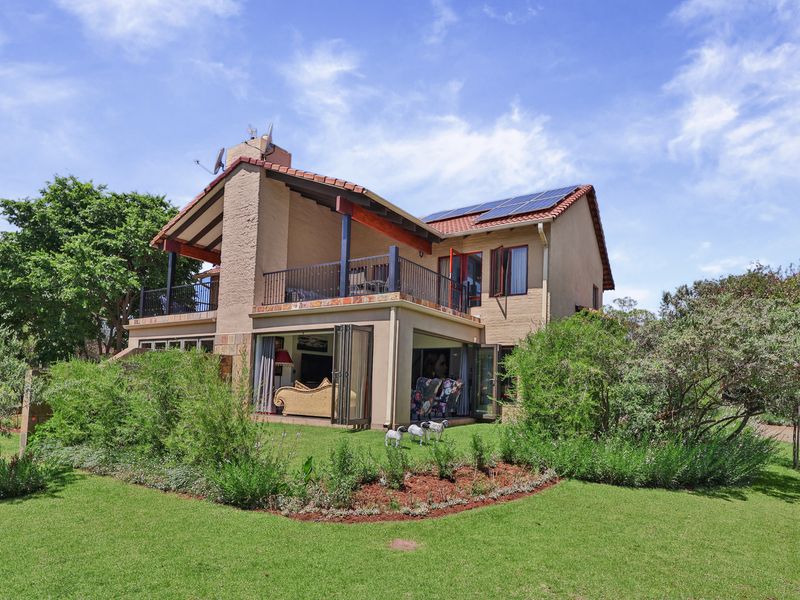Rear view of a two-story townhouse featuring a balcony, bi-fold doors opening to the garden, and roof-mounted solar panels.