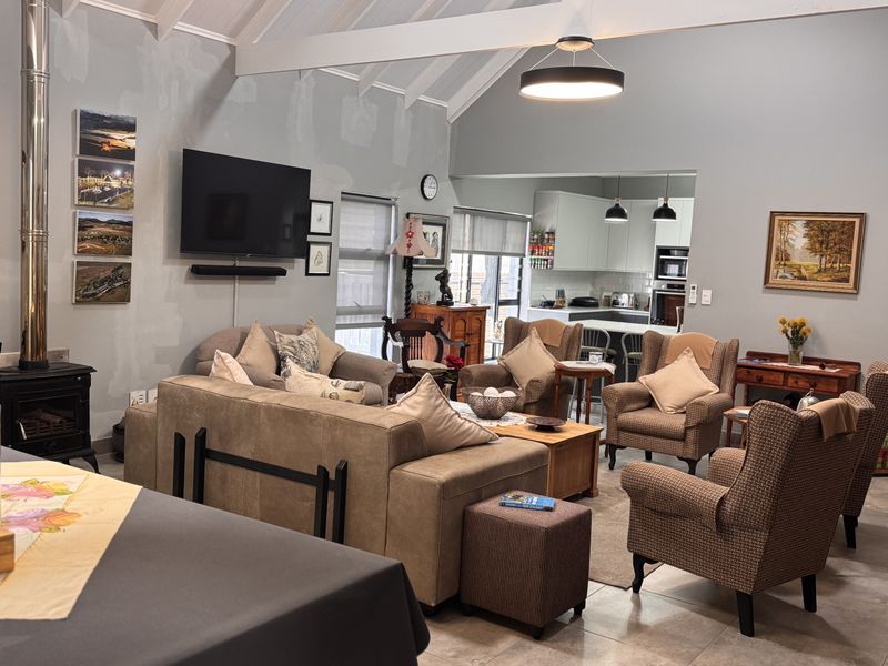 Spacious open-plan living area featuring a vaulted ceiling with exposed beams, a wood-burning stove, and a modern kitchen with an island.