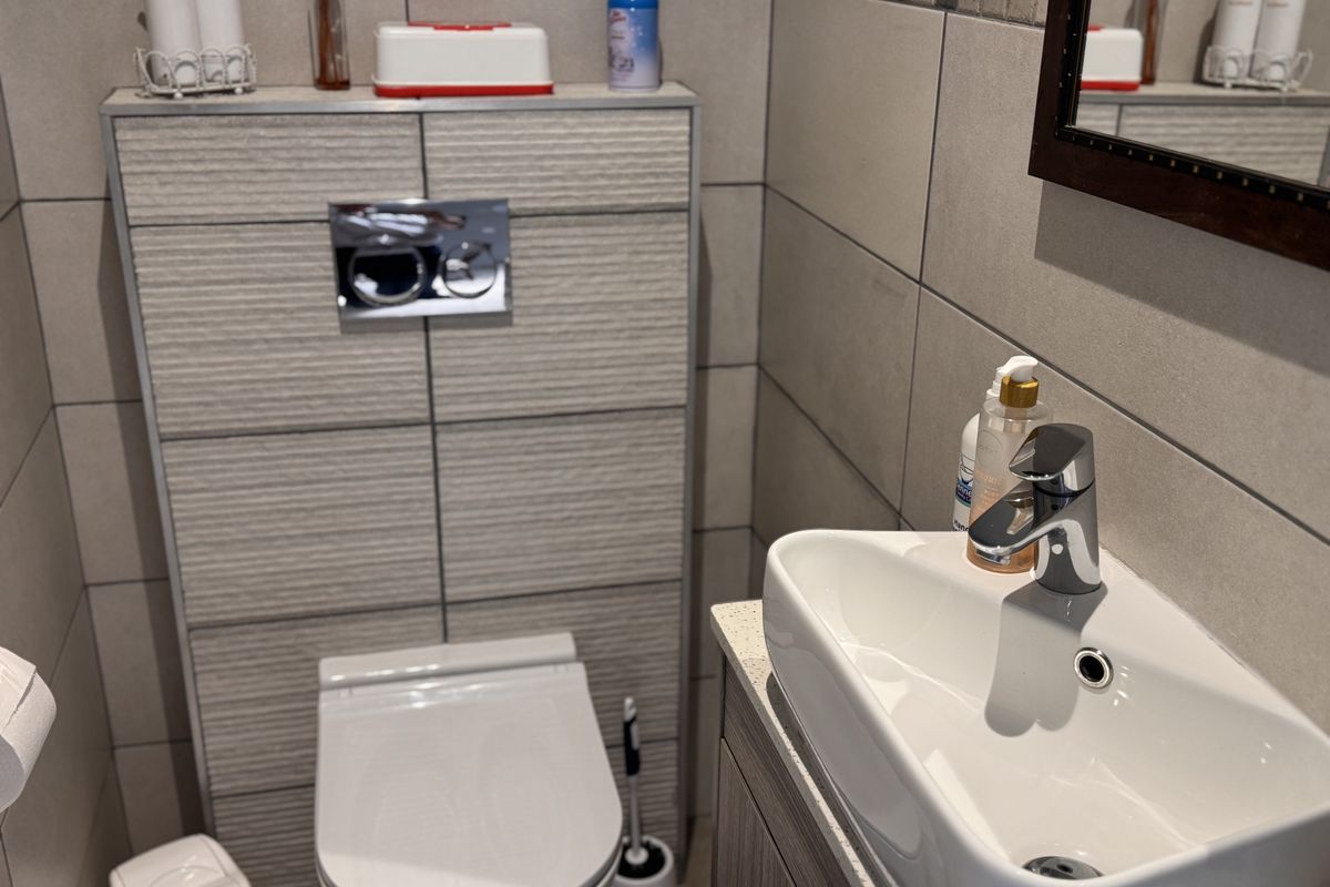 A modern bathroom featuring a wall-hung toilet with a concealed cistern, tiled walls, and a sleek vanity basin with a mixer tap.