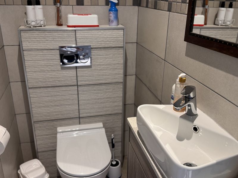 A modern bathroom featuring a wall-hung toilet with a concealed cistern, tiled walls, and a sleek vanity basin with a mixer tap.
