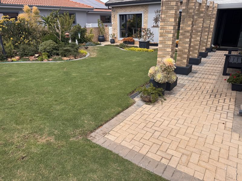 A well-maintained covered patio area featuring brick paving and structural brick pillars, overlooking a neatly landscaped garden with established plants.