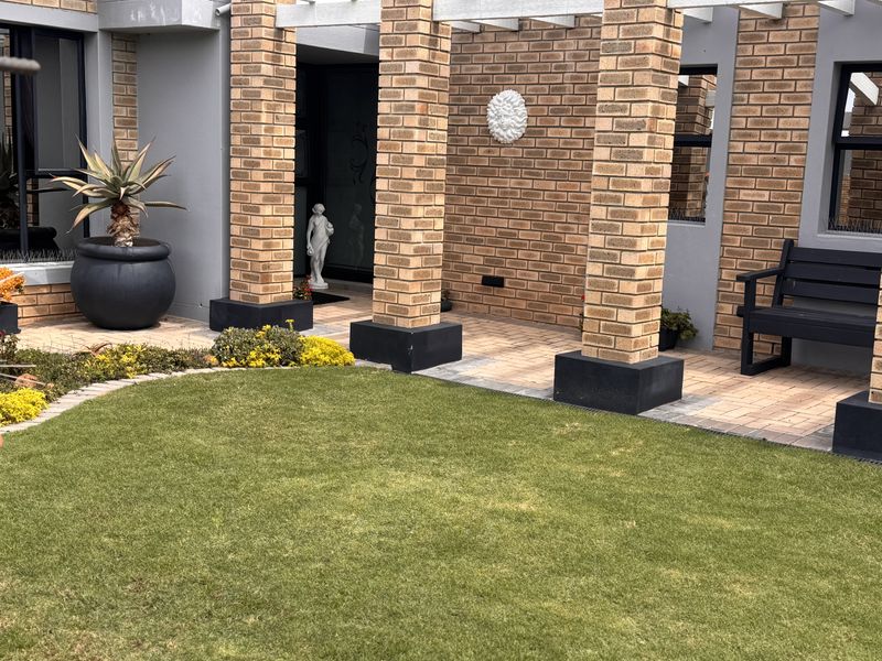 A well-maintained covered patio area featuring brick columns, a pergola structure, and paved flooring, overlooking a neat garden space.