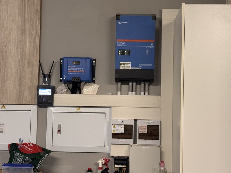 A well-organized utility area featuring a professional solar power installation, including a Victron inverter, charge controller, and integrated electrical distribution and combiner boxes.