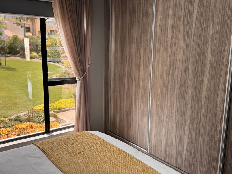 A well-maintained bedroom featuring large built-in wooden wardrobes and a window offering a pleasant view of the garden.