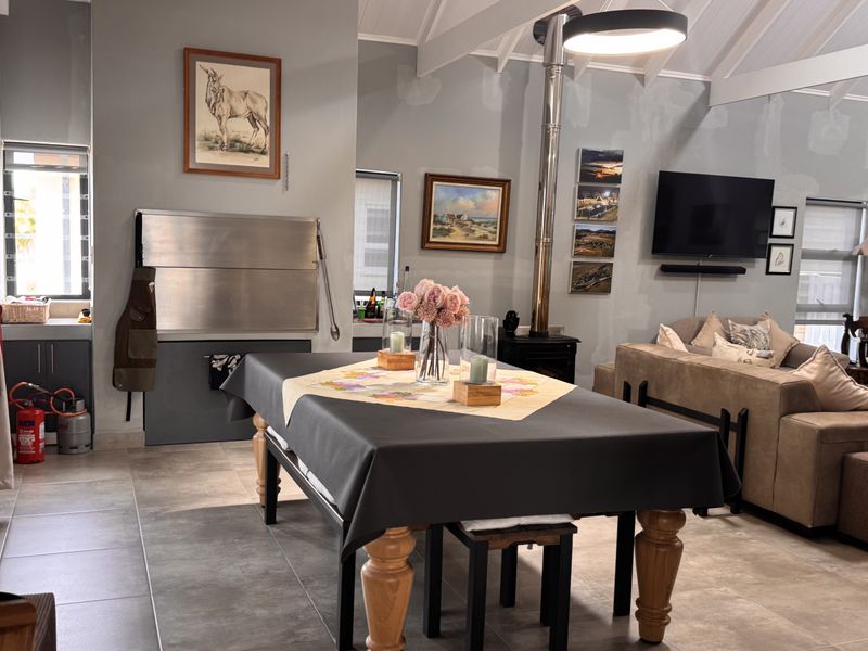 Open-plan living area featuring a built-in braai, freestanding fireplace, and vaulted ceilings, with tiled flooring throughout.