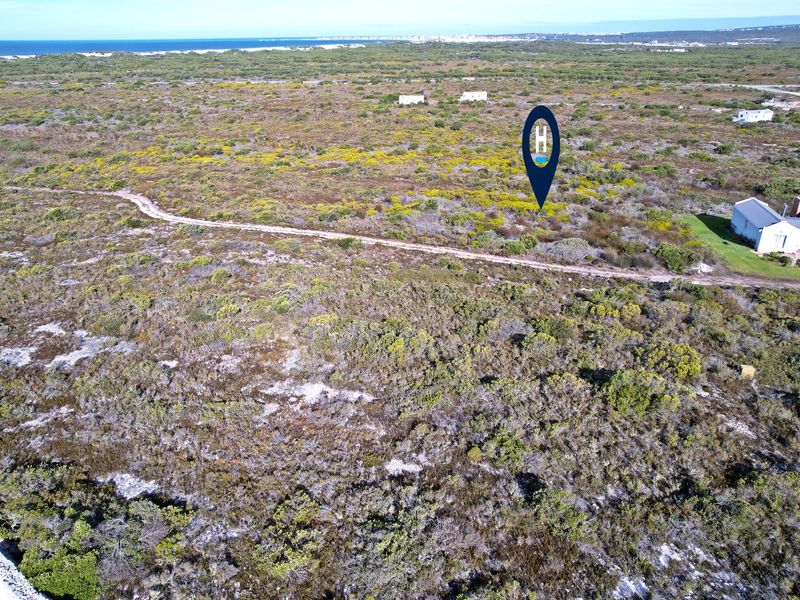 Aerial view of a vacant residential plot featuring native coastal vegetation and an unpaved access track, with distant ocean views.