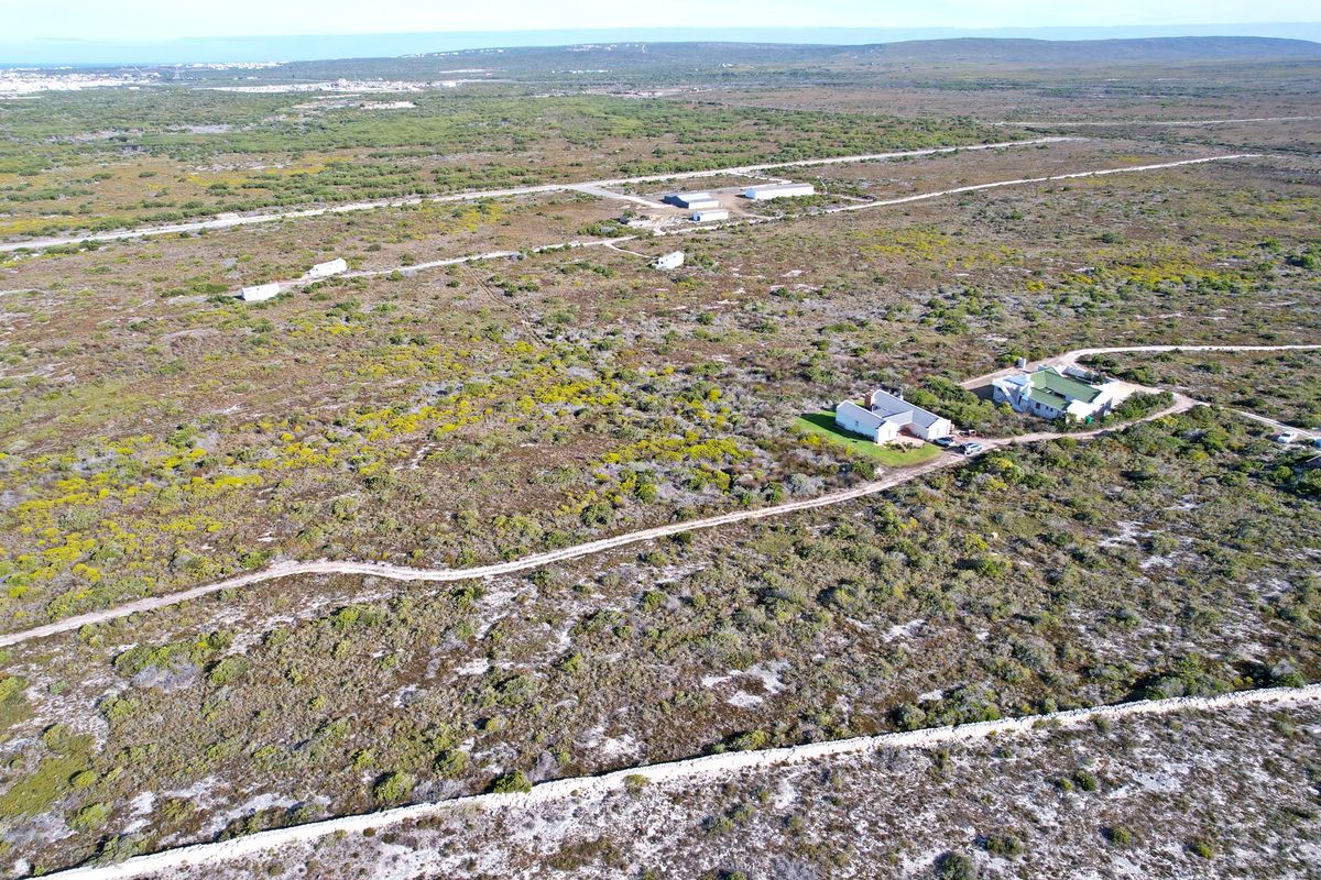 Aerial view of a large residential vacant land plot featuring natural vegetation, gravel access paths, and existing residential structures.