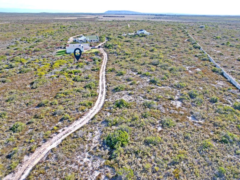 Aerial view of a large residential vacant land plot featuring natural vegetation, an unpaved access road, and existing stone boundary walling.