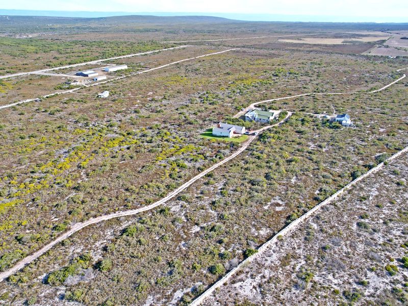 An aerial view of a large residential plot featuring natural vegetation, existing dwellings, and a dirt access road.