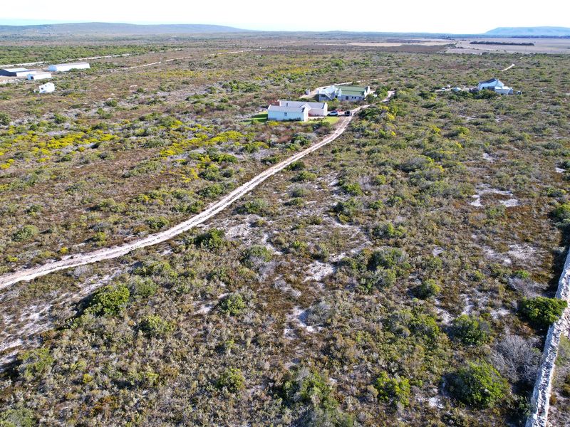 An aerial view of a large residential vacant land plot featuring natural fynbos vegetation, a dirt access road, and a stone boundary wall.