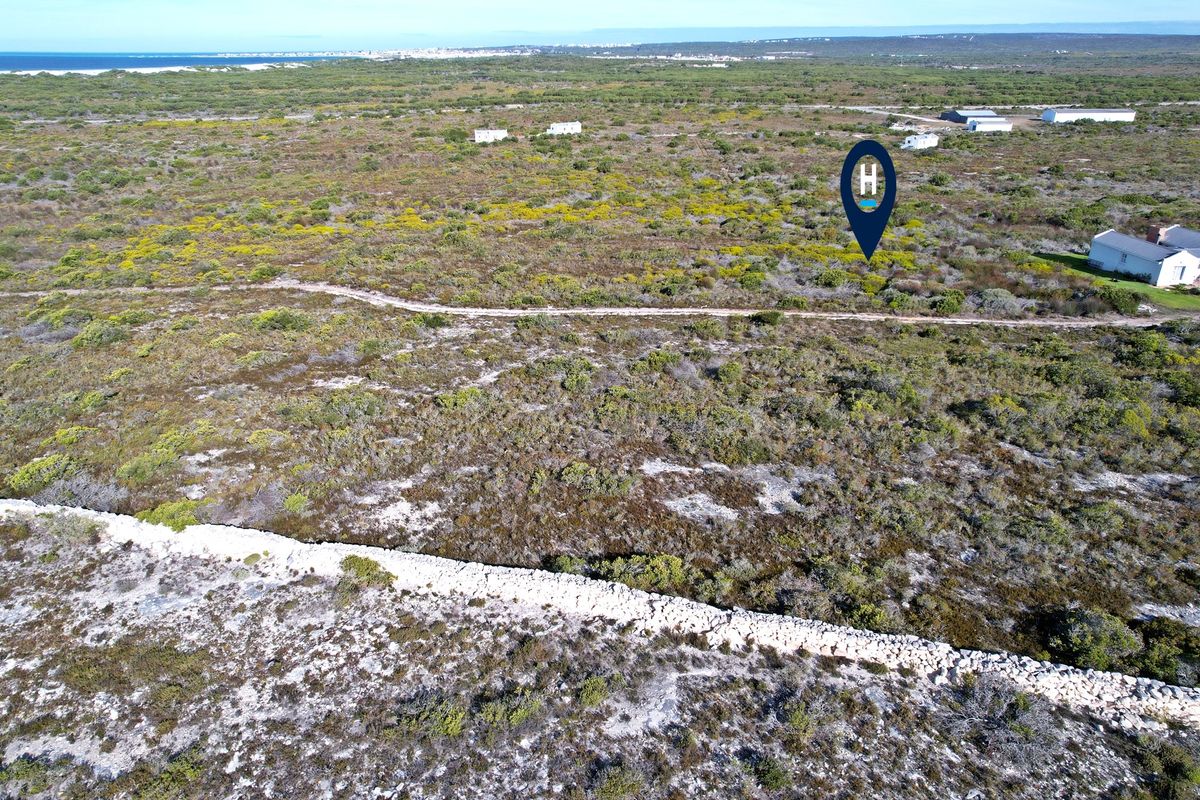 Aerial view of a vacant residential plot featuring natural coastal vegetation, a stone boundary wall, and an unpaved access track.