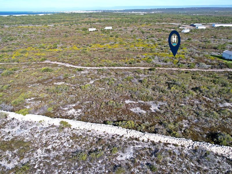 Aerial view of a vacant residential plot featuring natural coastal vegetation, a stone boundary wall, and an unpaved access track.