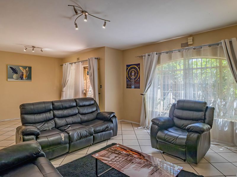 Spacious living room featuring tiled flooring, track lighting, and large arched windows with security bars, offering a bright and functional living space.