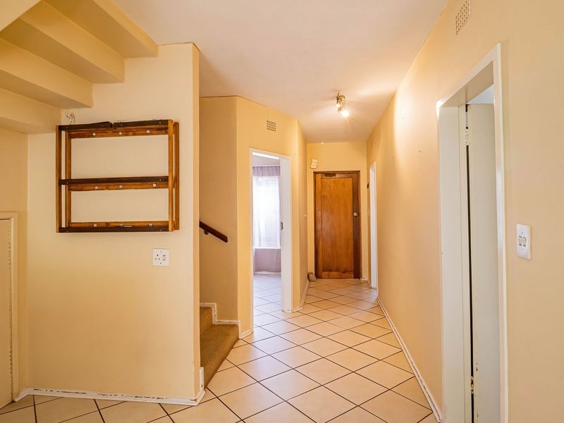 A spacious hallway featuring tiled flooring, a staircase, and access to multiple rooms, presenting a neutral canvas for interior updates.
