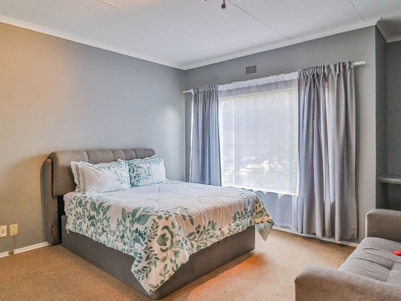 A well-lit bedroom featuring neutral wall tones, carpeted flooring, and a large window with installed curtain tracks.