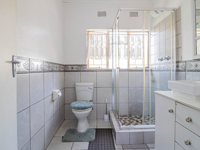 A functional bathroom featuring a glass-enclosed shower, a vanity with a basin, and neutral wall and floor tiling.