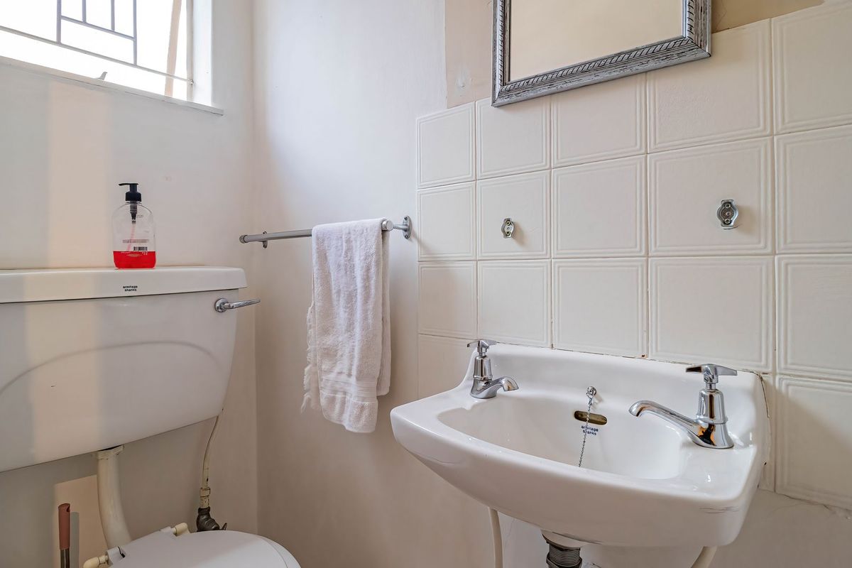 A compact bathroom featuring a wall-mounted basin, ceramic toilet, and tiled splashback, requiring cosmetic updates to improve its overall condition and aesthetic appeal.