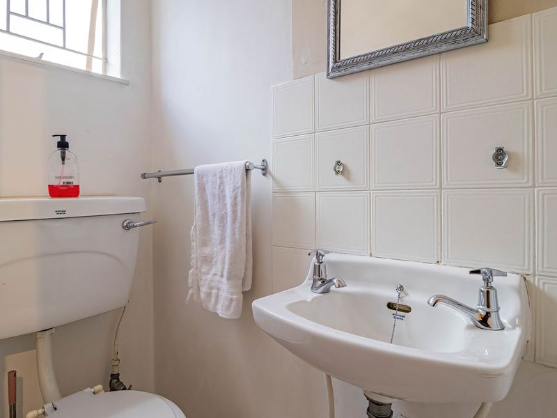 A compact bathroom featuring a wall-mounted basin, ceramic toilet, and tiled splashback, requiring cosmetic updates to improve its overall condition and aesthetic appeal.