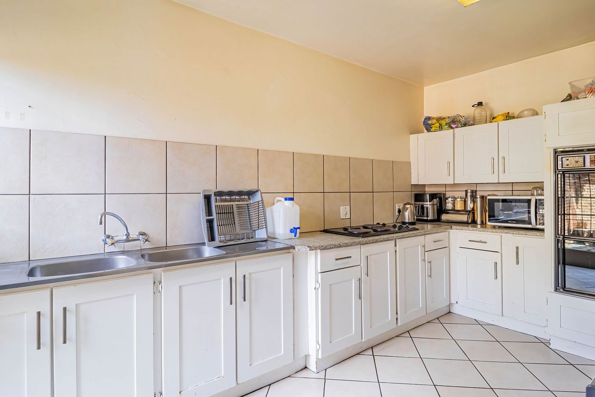 Functional kitchen featuring white cabinetry, tiled backsplash, double sink, built-in oven, and gas hob with tiled flooring throughout.
